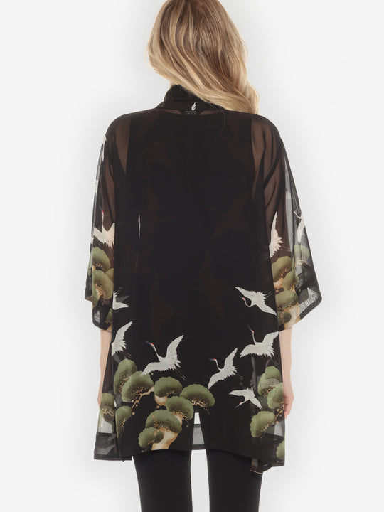 Woman wearing a black kimono-style garment with nature-themed design on a white background